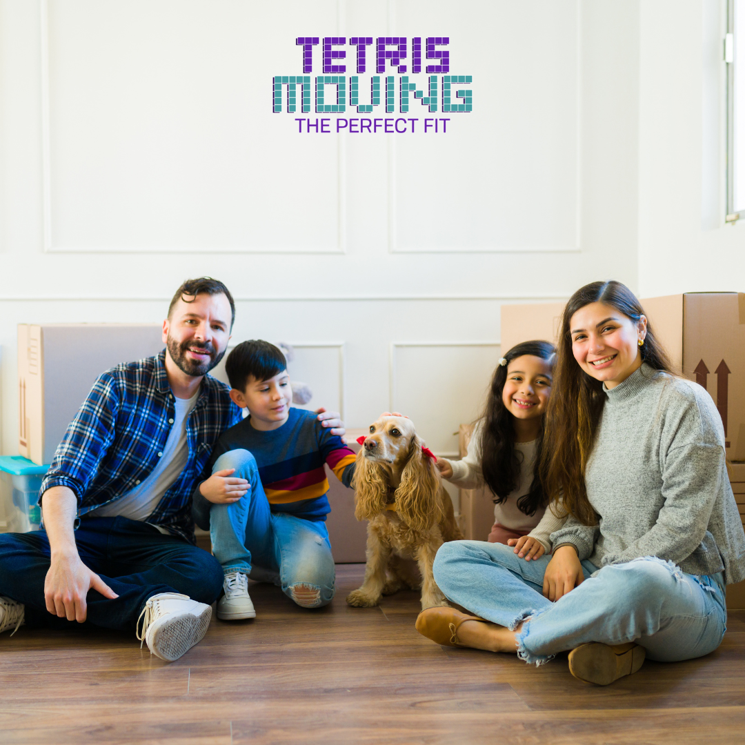 Family of 4 plus a dog sitting on a hardwood floor in front of moving boxes
